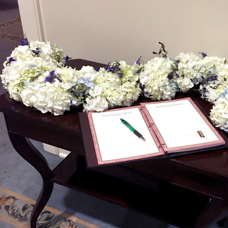 Guest book table with a white flower arrangement at a funeral, offering a peaceful and elegant tribute space for guests.