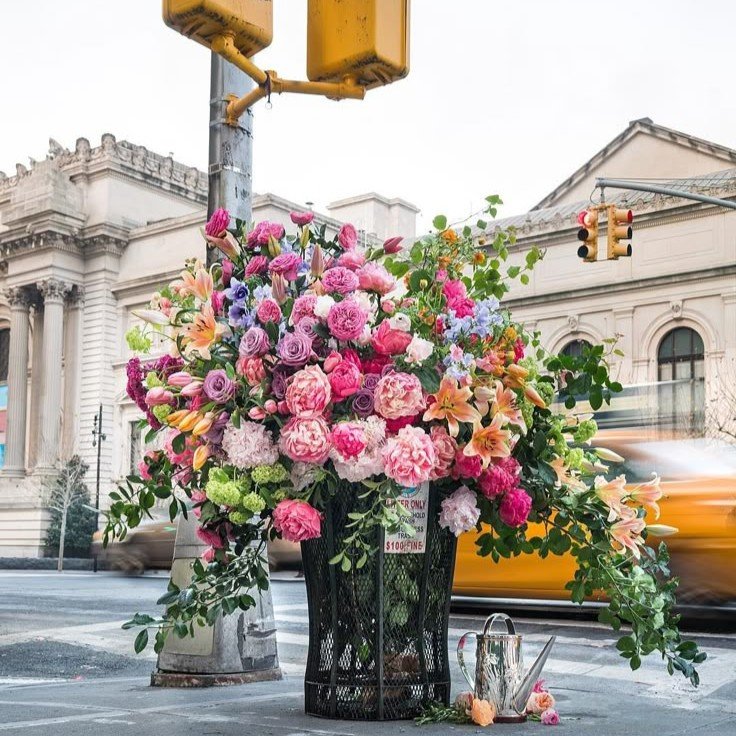 Massive, stunning floral arrangement creatively displayed in a trash can, blending elegance with unexpected design flair.