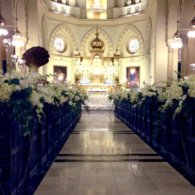 White flowers lining church pews leading to the altar for a romantic wedding ceremony.