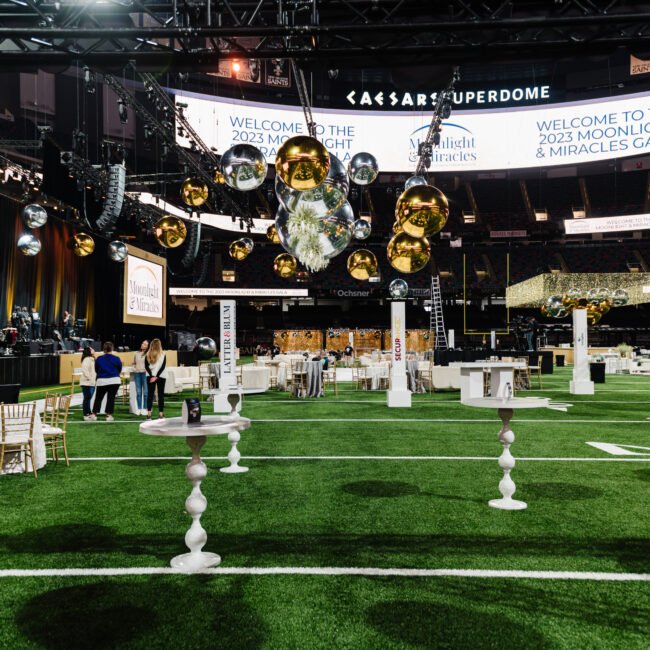 White floral arrangements and cocktail tables beneath metallic spheres on the Superdome field.