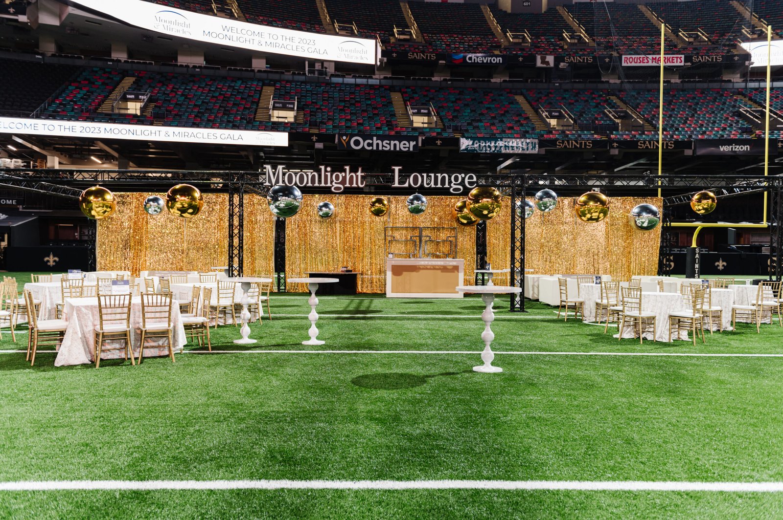 Moonlight Lounge at the Superdome with gold curtains, hanging metallic spheres, white cocktail tables and gold chairs.