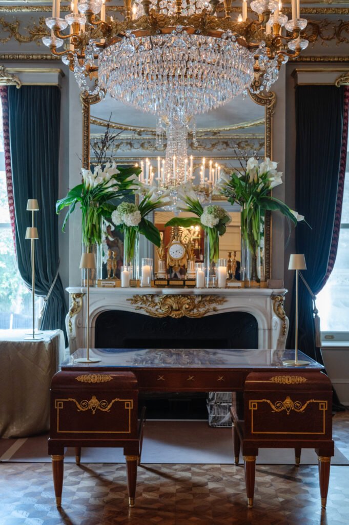 White flowers and greenery decorating a mantel beneath an ornate mirror.