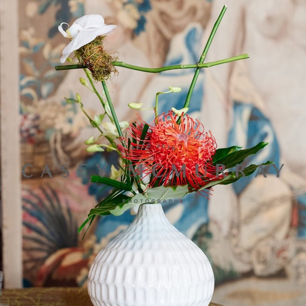 Red pincushion bloom, white flowers and branching stems in a ribbed white vase.