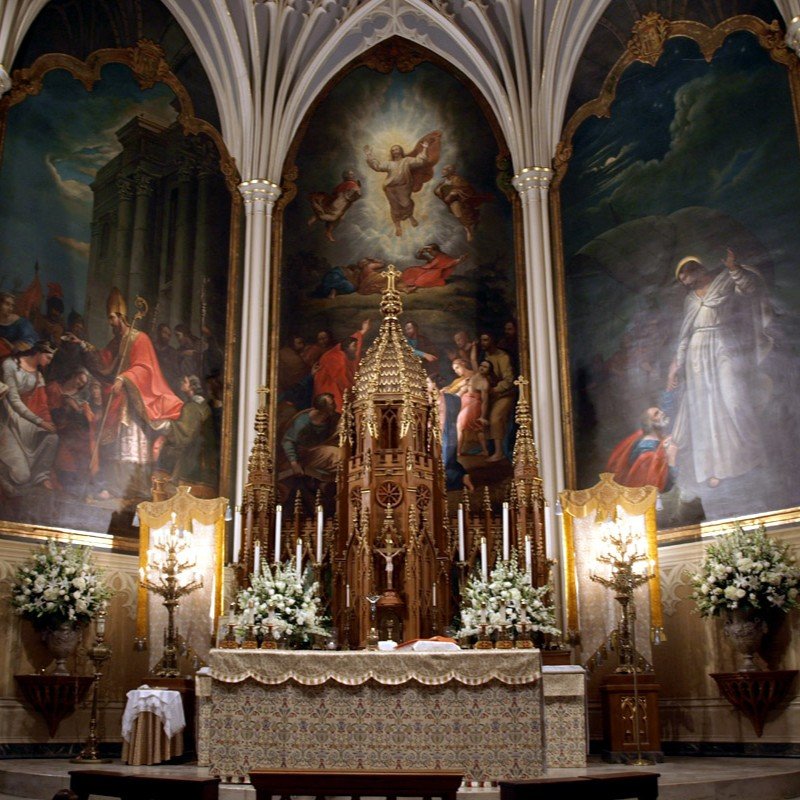 White floral arrangements decorating an ornate church altar beneath religious paintings.