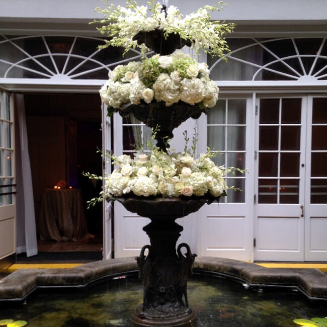 White flowers and greenery cascading over a tiered courtyard fountain.