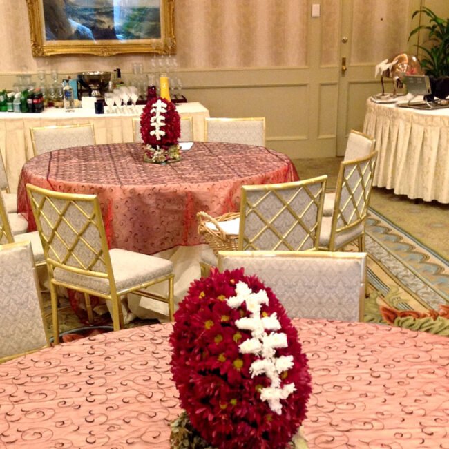 Football-shaped red floral centerpiece with white laces on a reception table.