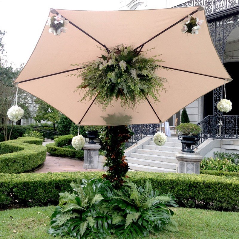 White flowers and greenery decorating the center of a garden umbrella.