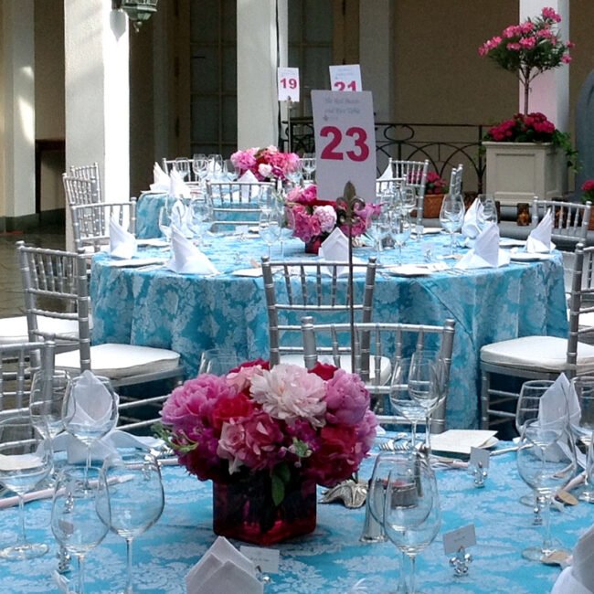 Pink floral centerpieces on blue reception tables with clear chairs.