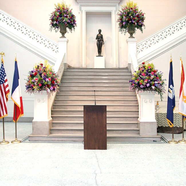 Large floral arrangements flanking a sweeping white staircase and a lectern.