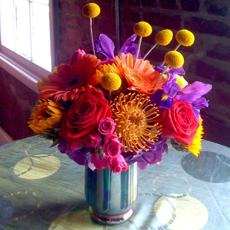 Orange, pink and purple flowers with yellow spherical accents in a small vase.