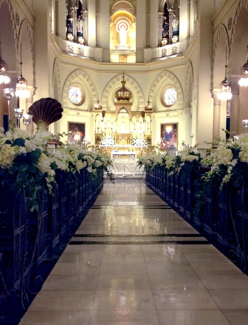 White floral arrangements lining the center aisle of a church for a wedding ceremony.
