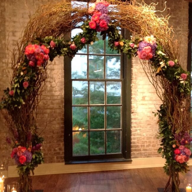 Pink and red flowers with greenery framing an arched window for a wedding ceremony.